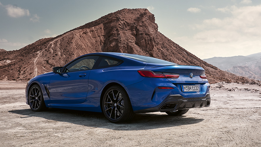 BMW Serije 8 Coupé M sport paket G15 LCI Facelift 2022 M Portimao plave metalik boje tročetvrtinski zadnji prikaz vozila parkiranog ispred stena