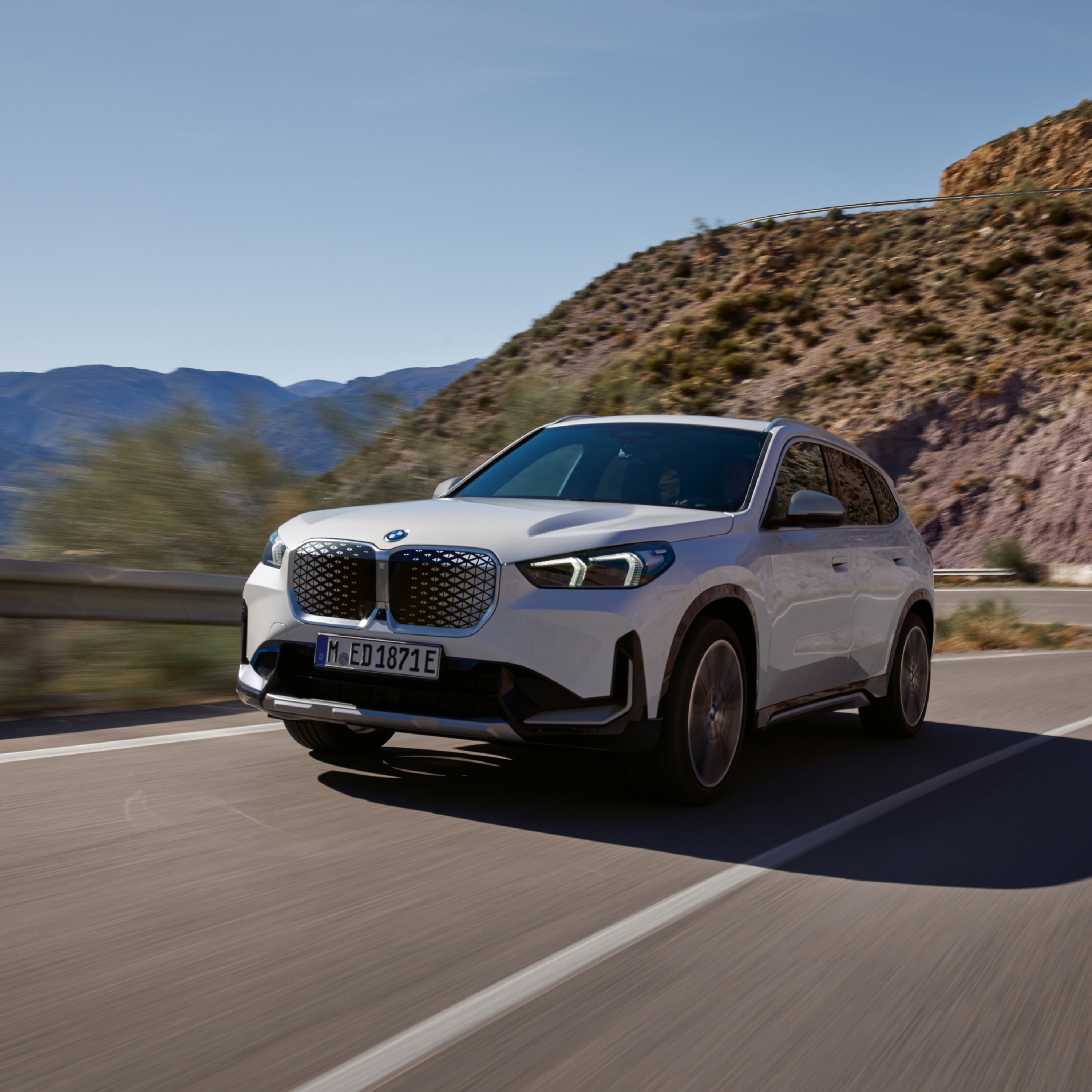 BMW iX1 Electric SUV Alpine bele boje tokom vožnje niz put kroz stenoviti planinski teren