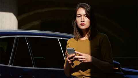 BMW ConnectedDrive pregled digitalnih usluga - žena sa pametnim telefonom ispred BMW-a.